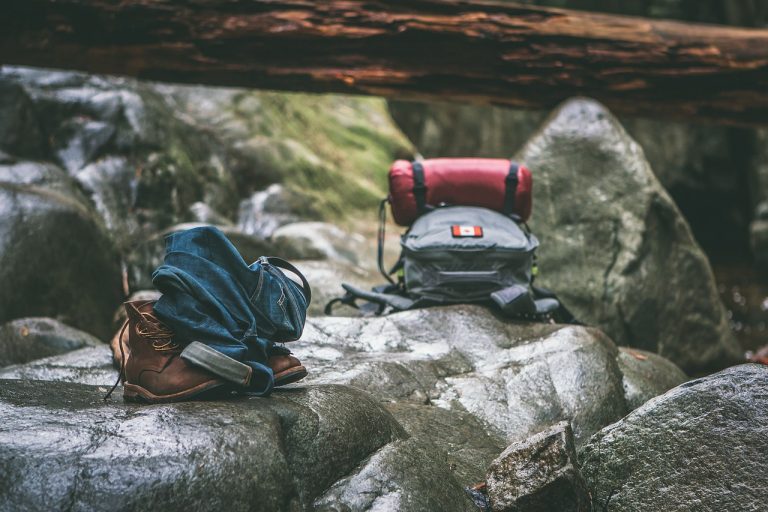 Backpack, hiking boots and walking stick on rocks - outdoor camping gear